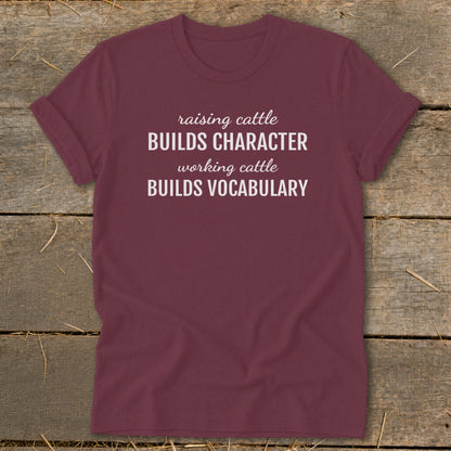Maroon t-shirt with white text: "raising cattle BUILDS CHARACTER, working cattle BUILDS VOCABULARY"