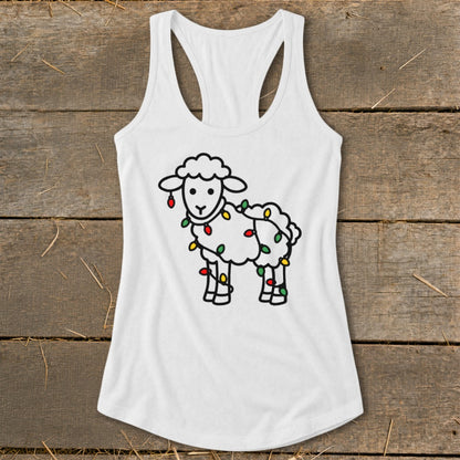 White racerback tank top featuring a cartoon sheep tangled in colorful Christmas lights, laid flat on wooden planks.