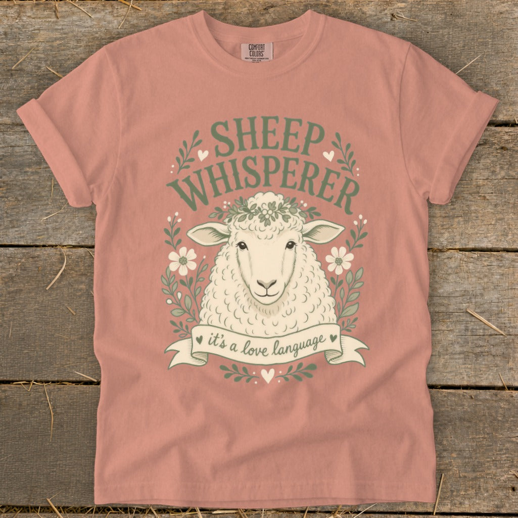 Peach t-shirt with "Sheep Whisperer" graphic and a sheep wearing a flower crown.
