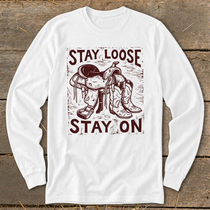 White long sleeve shirt with "STAY LOOSE STAY ON" text and saddle and boots graphic.