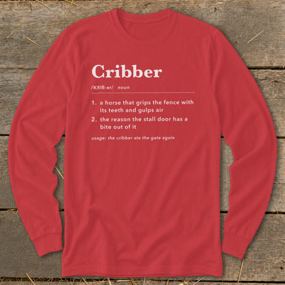 A red long-sleeve t-shirt with white text defining the word cribber laid on a wooden surface.