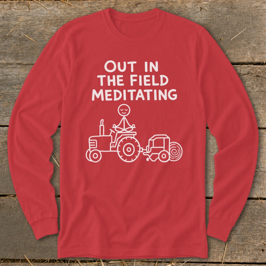 Red long sleeve shirt with white text "OUT IN THE FIELD MEDITATING" and a stick figure meditating on a tractor.