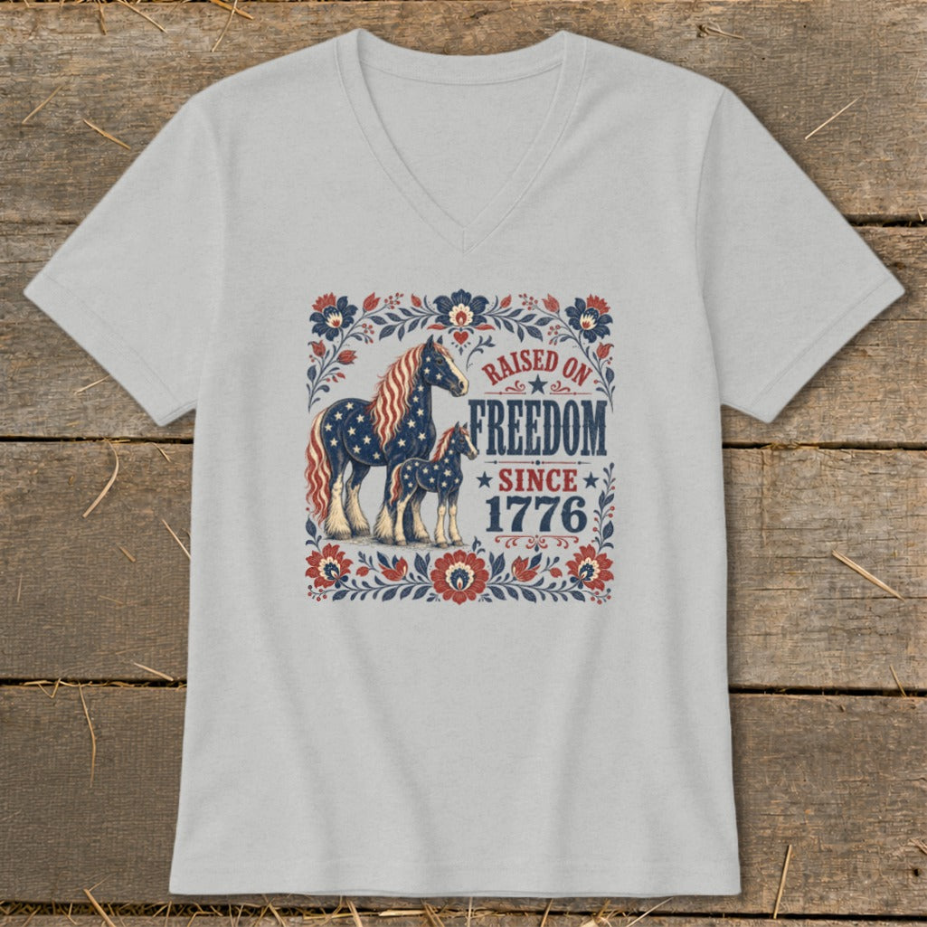 T-shirt graphic featuring two horses with American flag patterns and text "Raised on Freedom Since 1776".