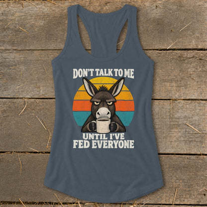 A dark gray racerback tank top featuring a graphic of a grumpy donkey holding a coffee mug in front of a retro sunset.