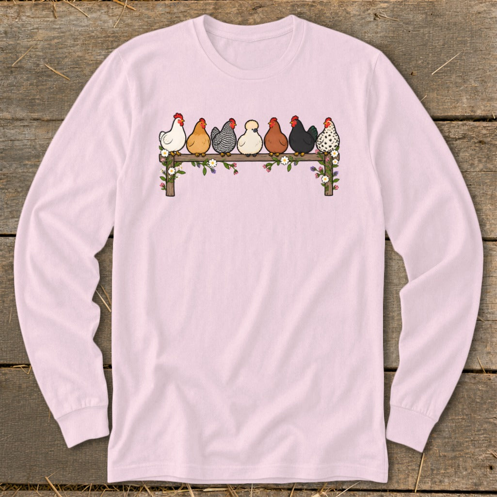 Light pink long-sleeve t-shirt featuring an illustration of seven colorful chickens perched on a flower-covered wooden fence.