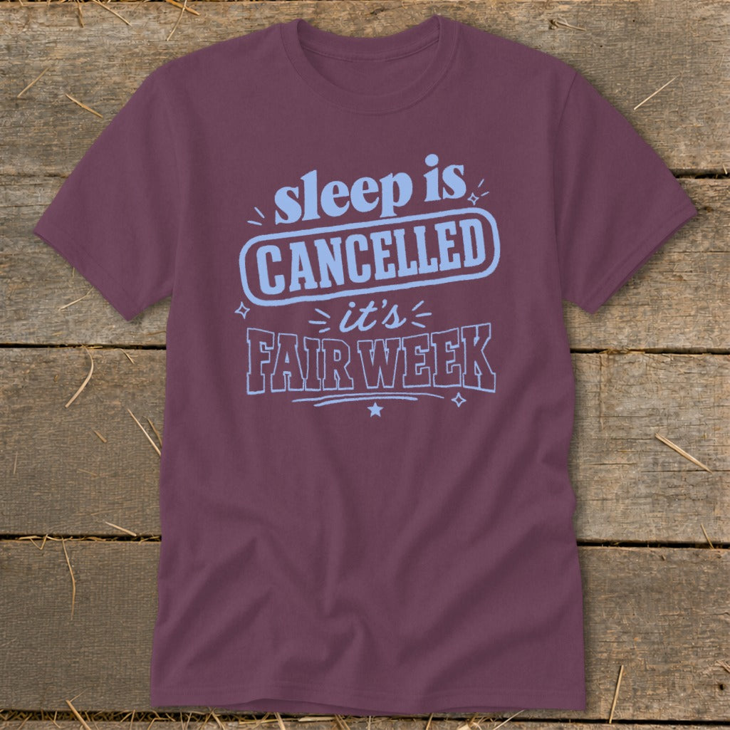 Maroon t-shirt with light blue text that reads "sleep is CANCELLED it's FAIR WEEK".