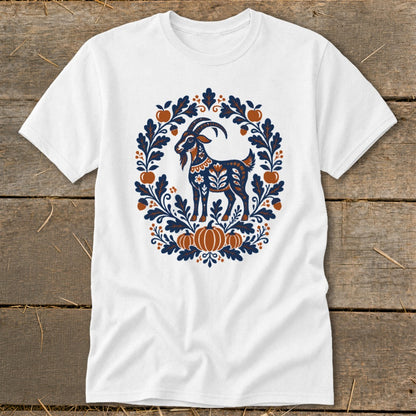 A white t-shirt featuring a blue and rust folk-art goat graphic surrounded by leaves, acorns, and pumpkins.
