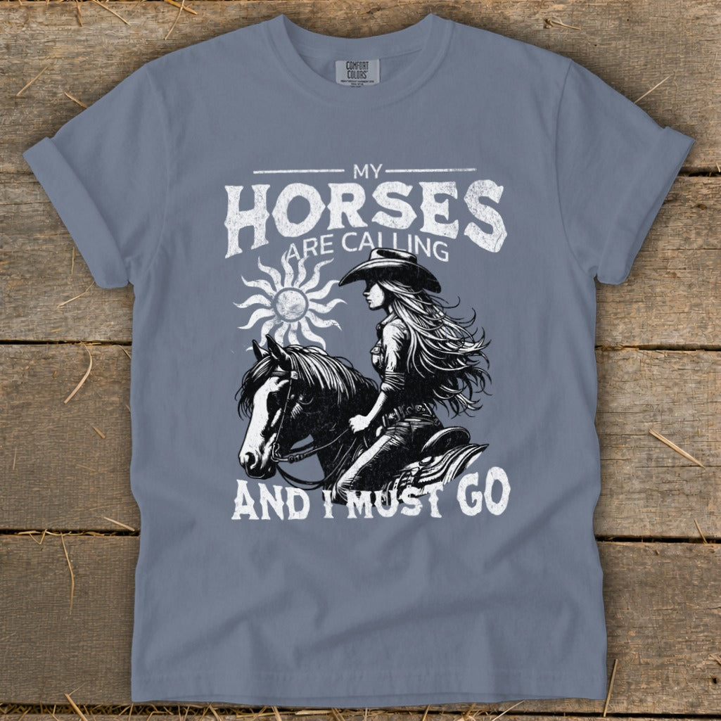 T-shirt graphic of a cowgirl riding a horse with text "My Horses Are Calling And I Must Go".