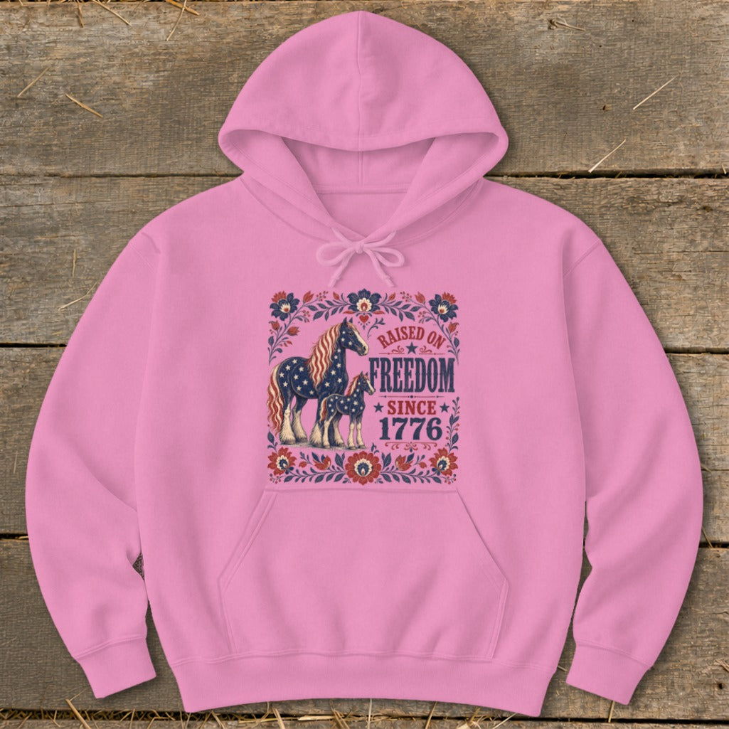 Pink hoodie with American flag pattern horses and "Raised on Freedom Since 1776" text.