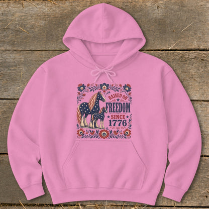 Pink hoodie with American flag pattern horses and "Raised on Freedom Since 1776" text.
