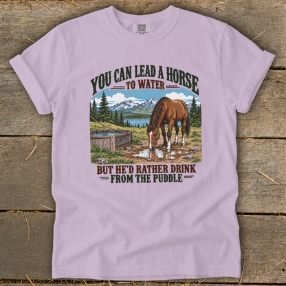 A light purple t-shirt featuring a graphic of a horse drinking from a puddle.
