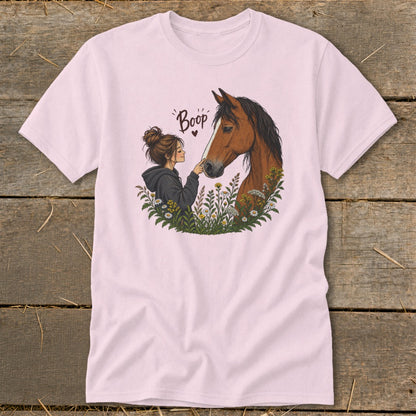 A light pink t-shirt featuring an illustration of a woman touching a horse's nose surrounded by flowers with the text "Boop".