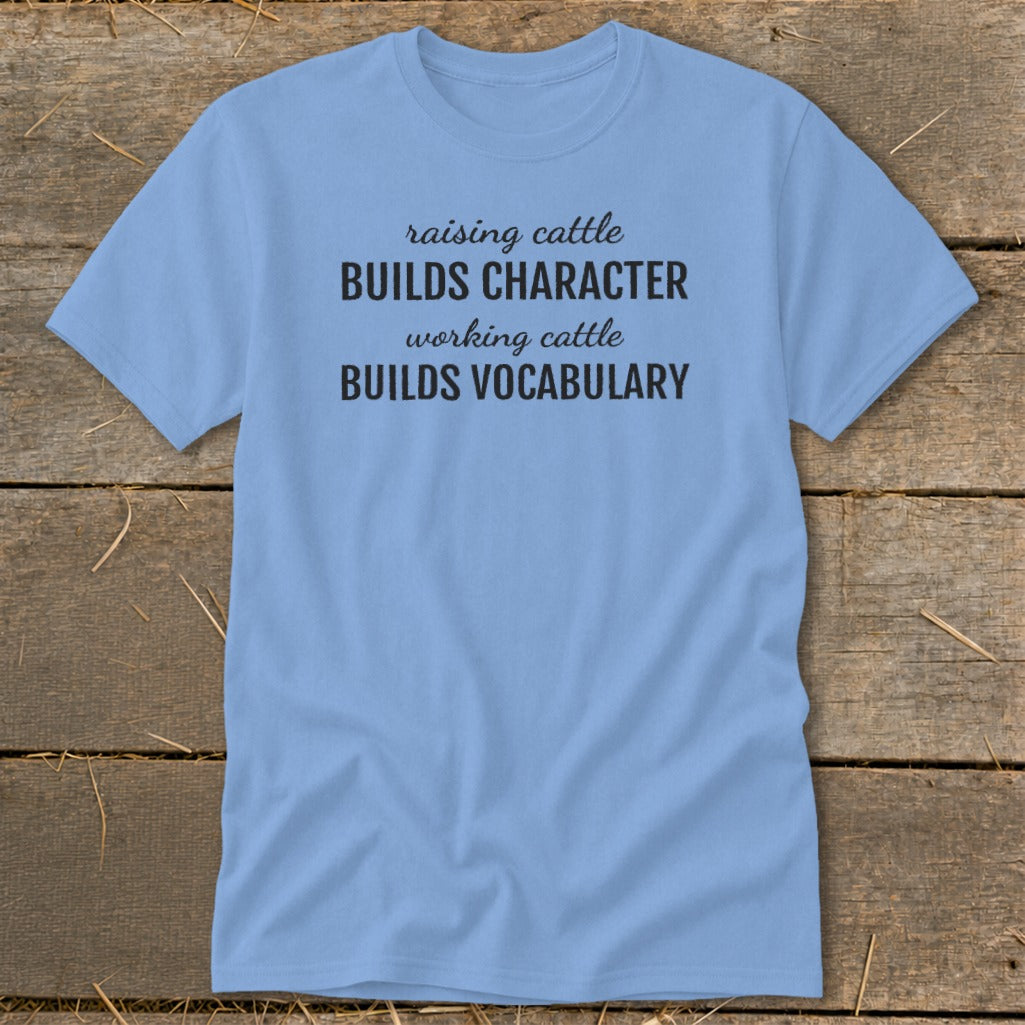 Light blue t-shirt with black text: "raising cattle BUILDS CHARACTER, working cattle BUILDS VOCABULARY."