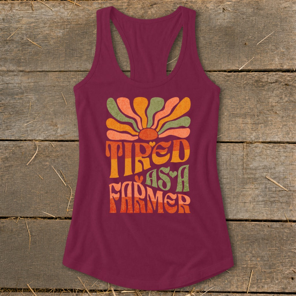 Burgundy tank top with "Tired As A Farmer" text and colorful retro sun graphic.
