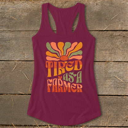 Burgundy tank top with "Tired As A Farmer" text and colorful retro sun graphic.