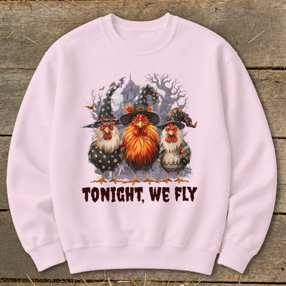 Three chickens in witch hats and Halloween costumes stand before a spooky mansion.