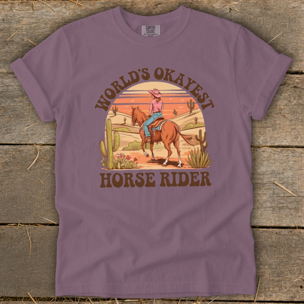 T-shirt graphic with desert scene, horse rider, and text "WORLD'S OKAYEST HORSE RIDER".