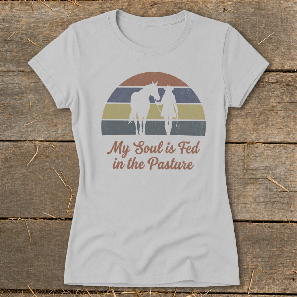 White t-shirt with graphic of horse and rider, sunset background, and text "My Soul is Fed in the Pasture".