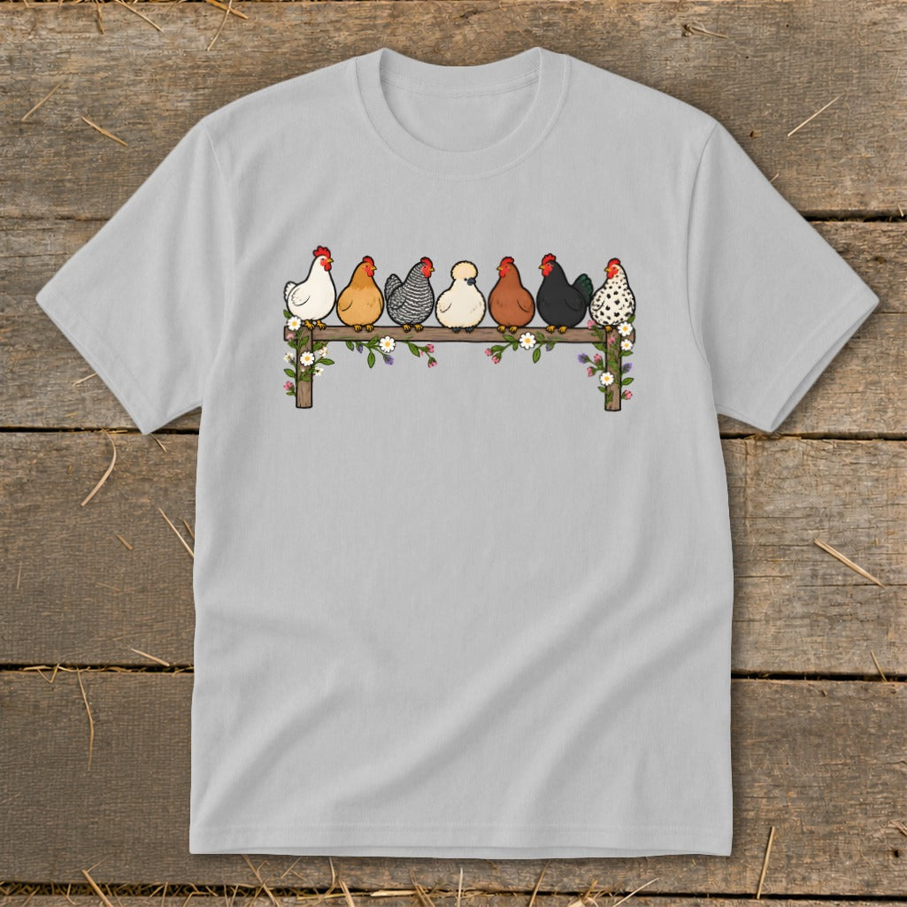 A light gray t-shirt featuring an illustration of seven colorful chickens perched on a flower-covered fence.