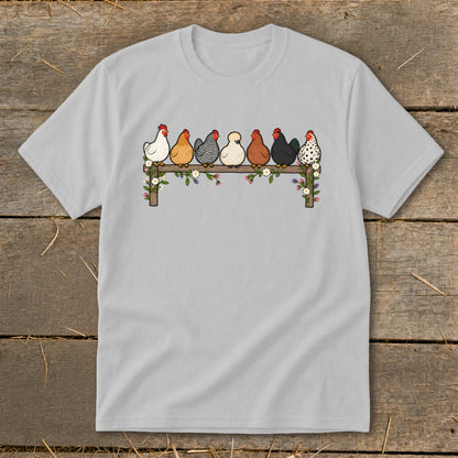 A light gray t-shirt featuring an illustration of seven colorful chickens perched on a flower-covered fence.