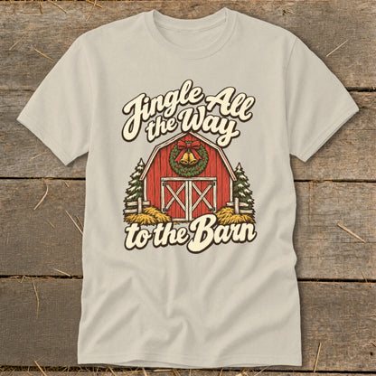 Light beige t-shirt with graphic of red barn, bells, wreath, and text "Jingle All the Way to the Barn".
