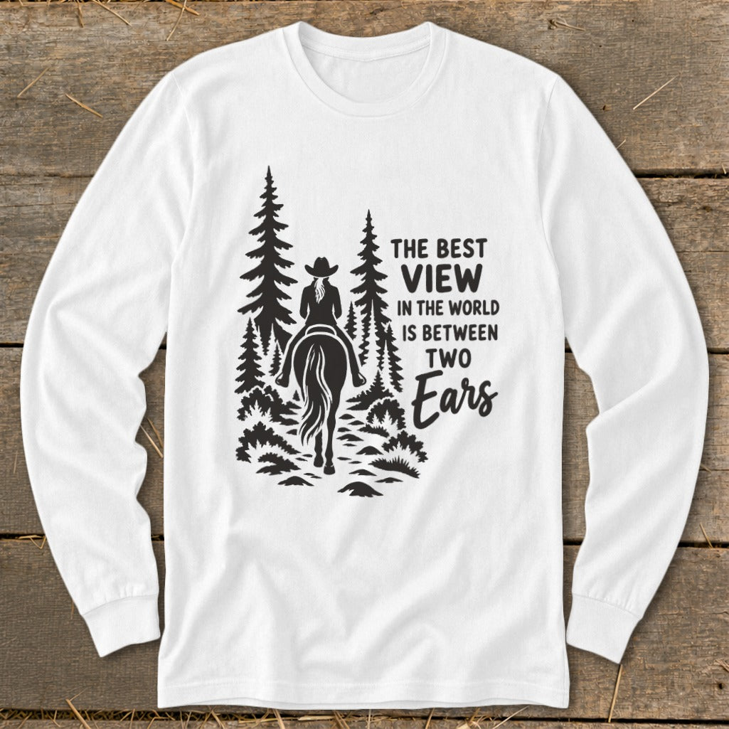 A white long-sleeved t-shirt features a black graphic of a horseback rider among pine trees with text that reads, "The best view in the world is between two ears."