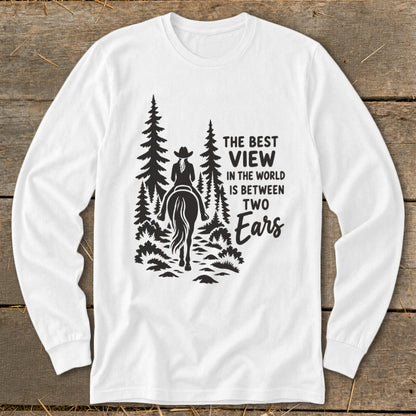A white long-sleeved t-shirt features a black graphic of a horseback rider among pine trees with text that reads, "The best view in the world is between two ears."