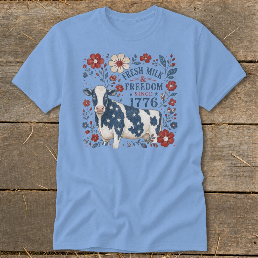 Light blue t-shirt with a cow wearing a flag pattern and text "Fresh Milk & Freedom Since 1776".
