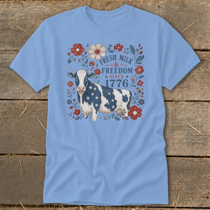 Light blue t-shirt with a cow wearing a flag pattern and text "Fresh Milk & Freedom Since 1776".