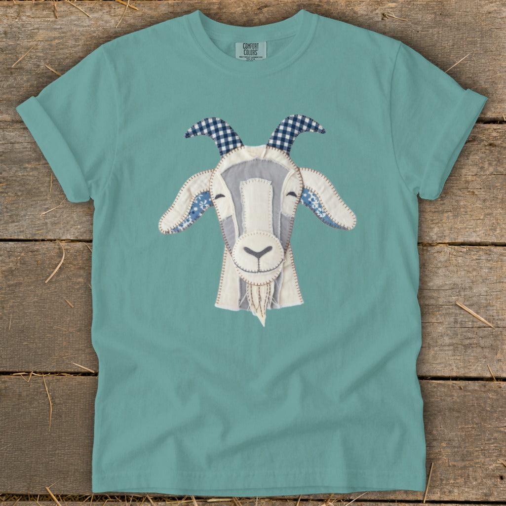 Teal t-shirt featuring a patchwork goat face with blue checkered horns and floral ears.