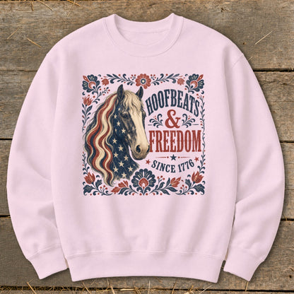 Light pink crewneck sweatshirt with horse and patriotic text "HOOFBEATS & FREEDOM SINCE 1776".
