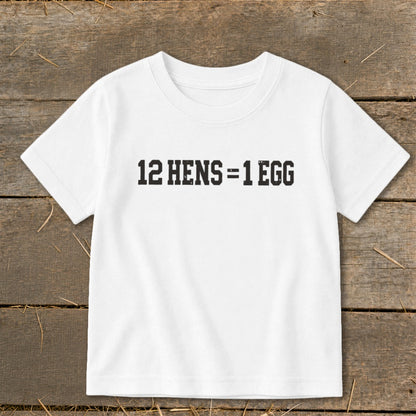 A white t-shirt featuring the black text 12 HENS = 1 EGG, laid flat on a rustic wooden background.