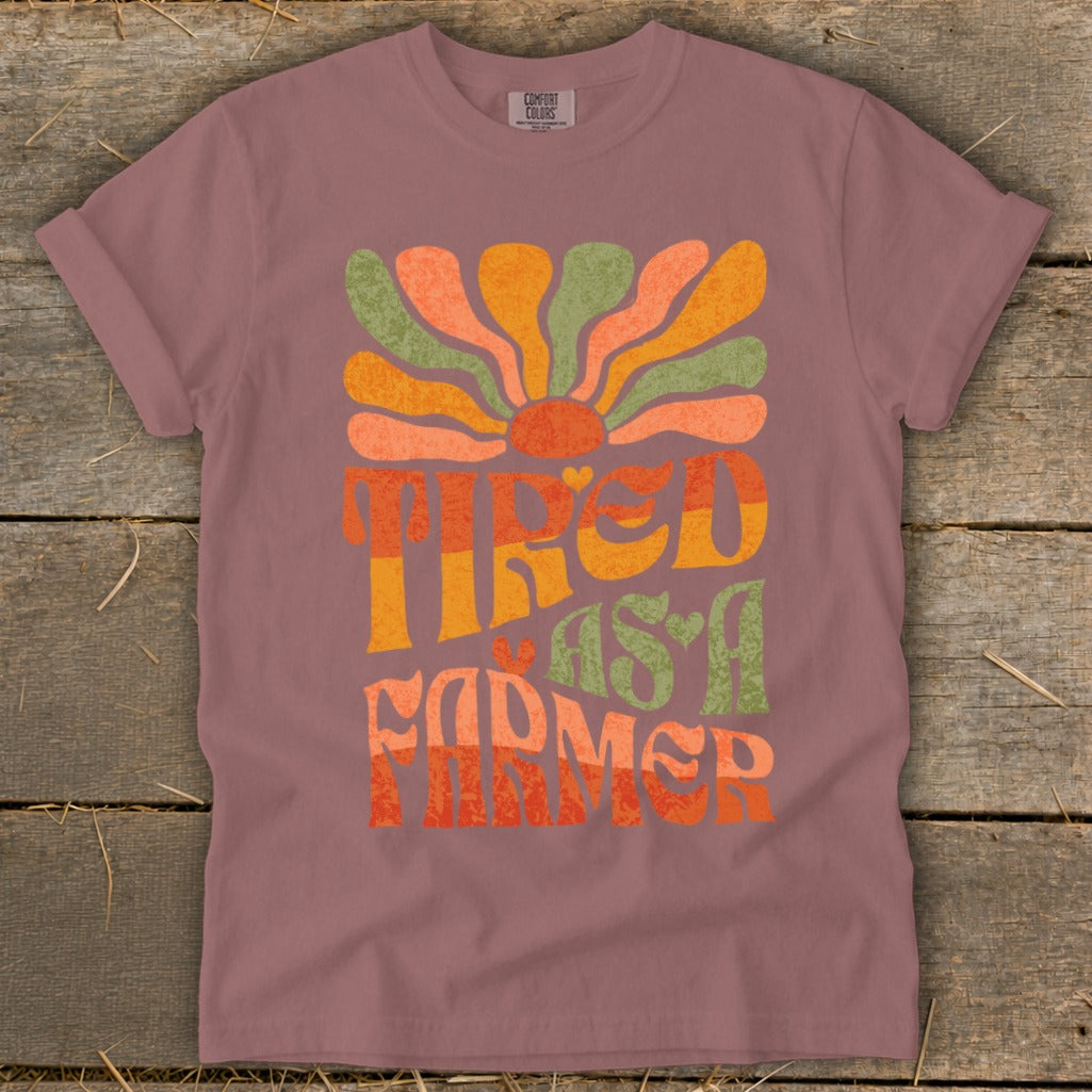 Tired as a Farmer text graphic with retro sunburst on muted pink t-shirt.
