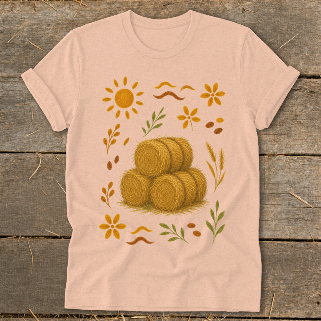 T-shirt with stacked hay bales, sun, flowers, and wheat illustrations.