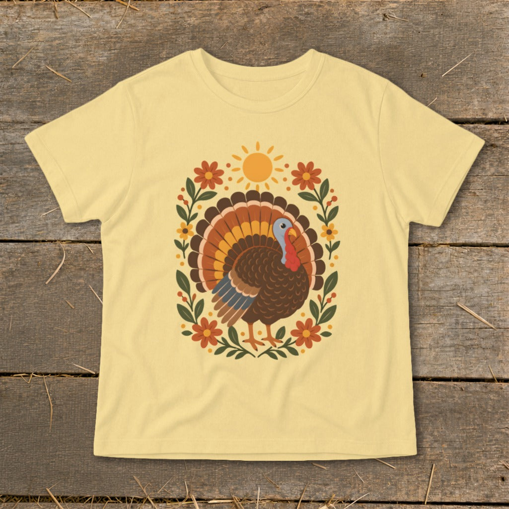 Light yellow t-shirt with a Thanksgiving turkey design surrounded by flowers and a sun.