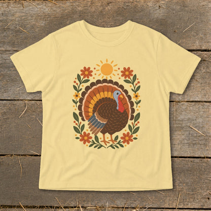 Light yellow t-shirt with a Thanksgiving turkey design surrounded by flowers and a sun.