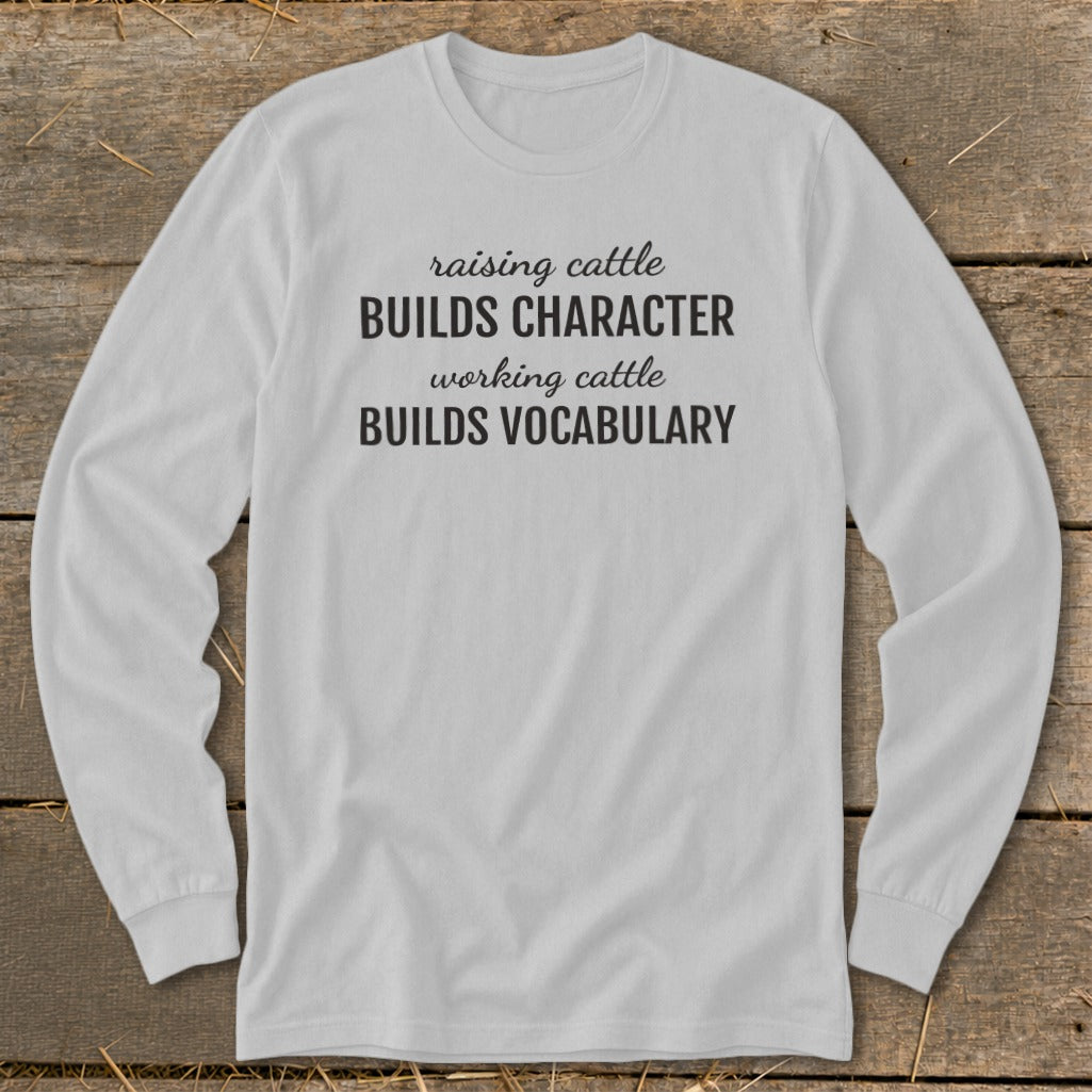 White long-sleeved shirt with black text "raising cattle BUILDS CHARACTER working cattle BUILDS VOCABULARY".