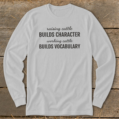 White long-sleeved shirt with black text "raising cattle BUILDS CHARACTER working cattle BUILDS VOCABULARY".