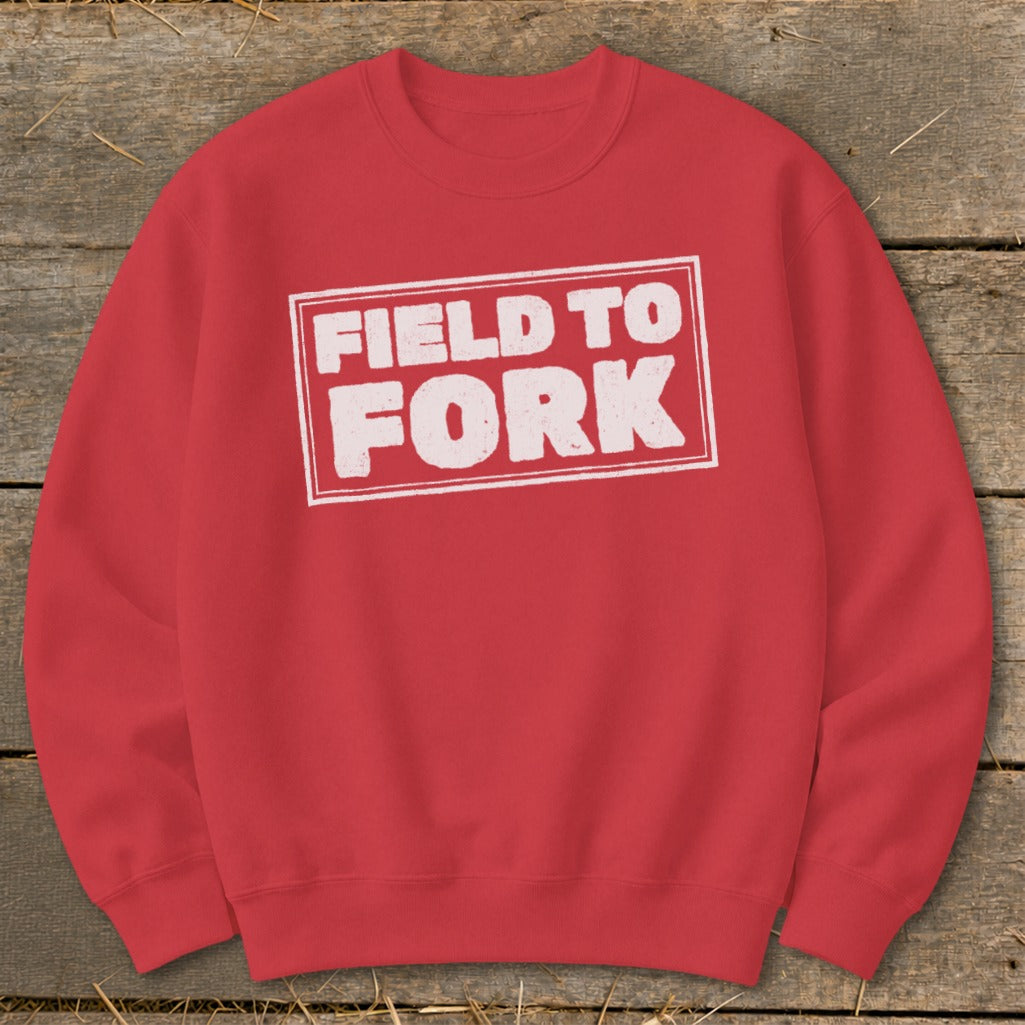 A red crewneck sweatshirt featuring a white rectangular graphic with the text "FIELD TO FORK."
