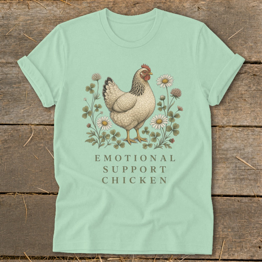 Light green t-shirt with a chicken illustration surrounded by clover and daisies, text "EMOTIONAL SUPPORT CHICKEN."