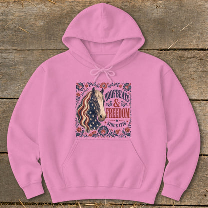Pink hoodie with a horse graphic featuring an American flag mane and text "Hoofbeats & Freedom Since 1776".