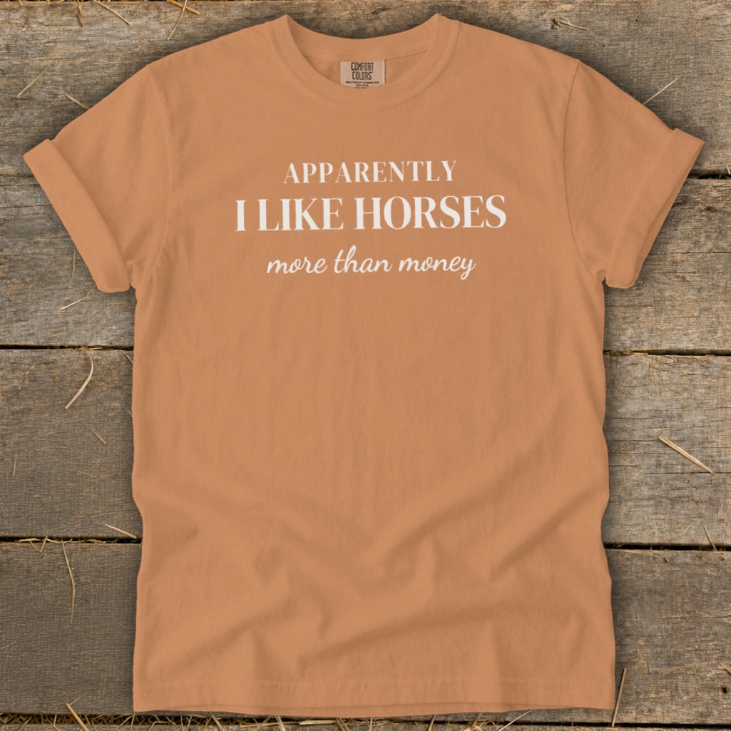 Orange t-shirt with white text reading "APPARENTLY I LIKE HORSES more than money".