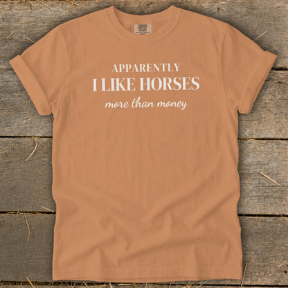 Orange t-shirt with white text reading "APPARENTLY I LIKE HORSES more than money".