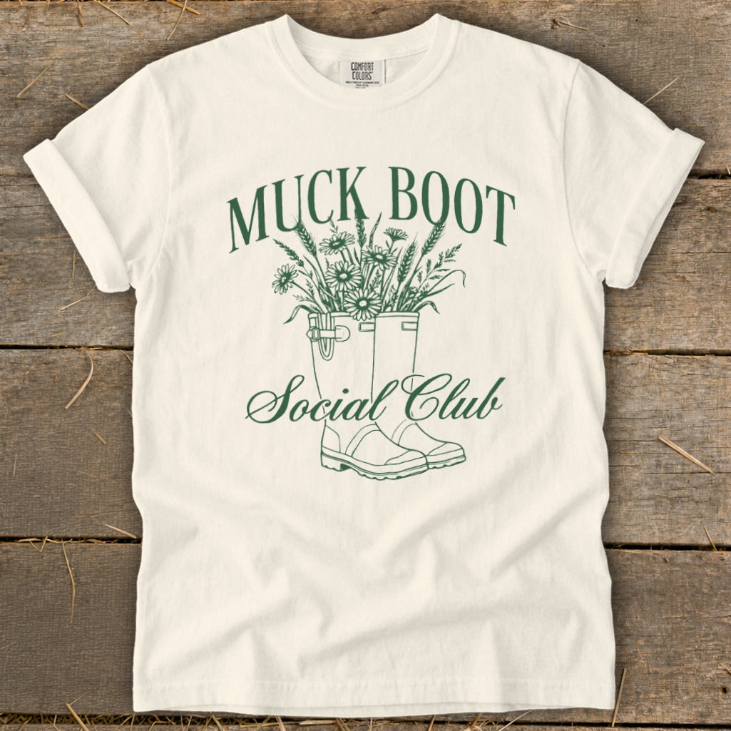 Cream t-shirt with "Muck Boot Social Club" text and floral-filled boots graphic.