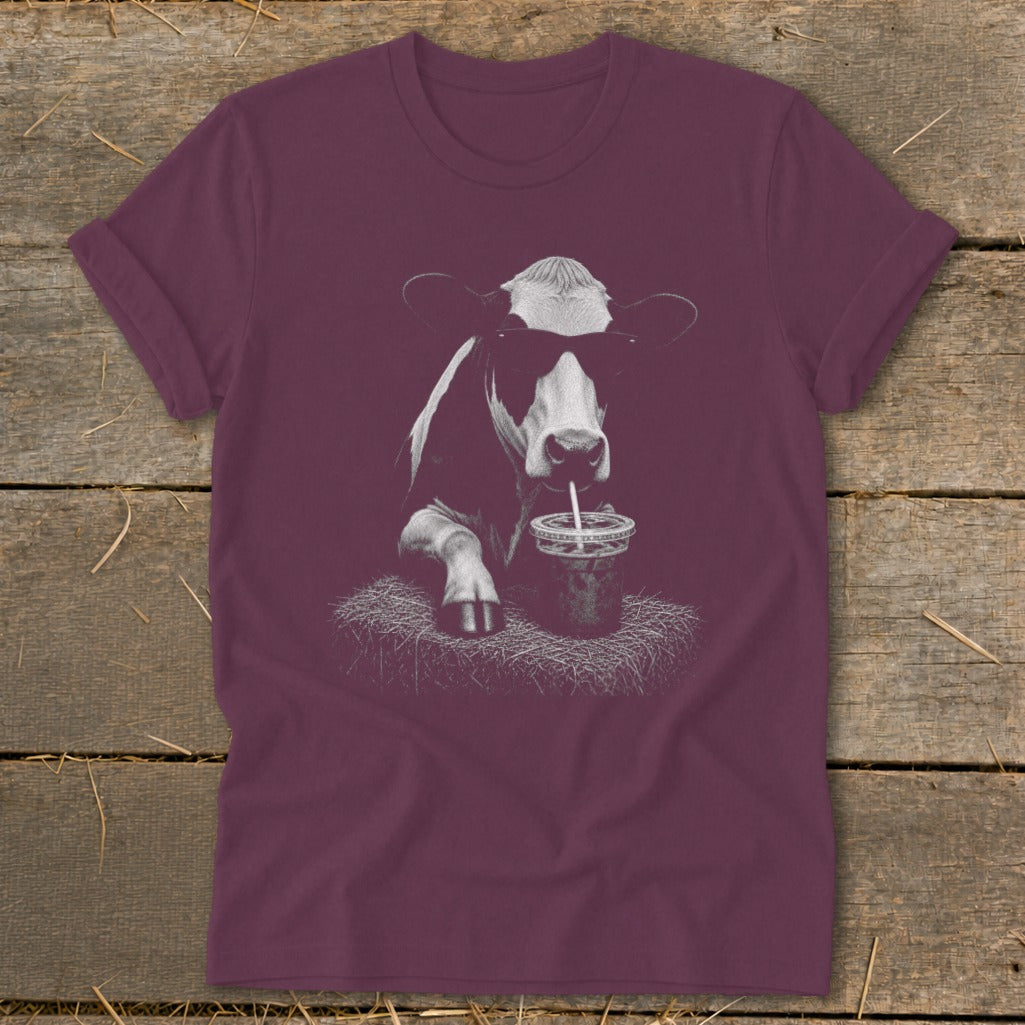 Black and white cow wearing sunglasses drinks from a cup with a straw.