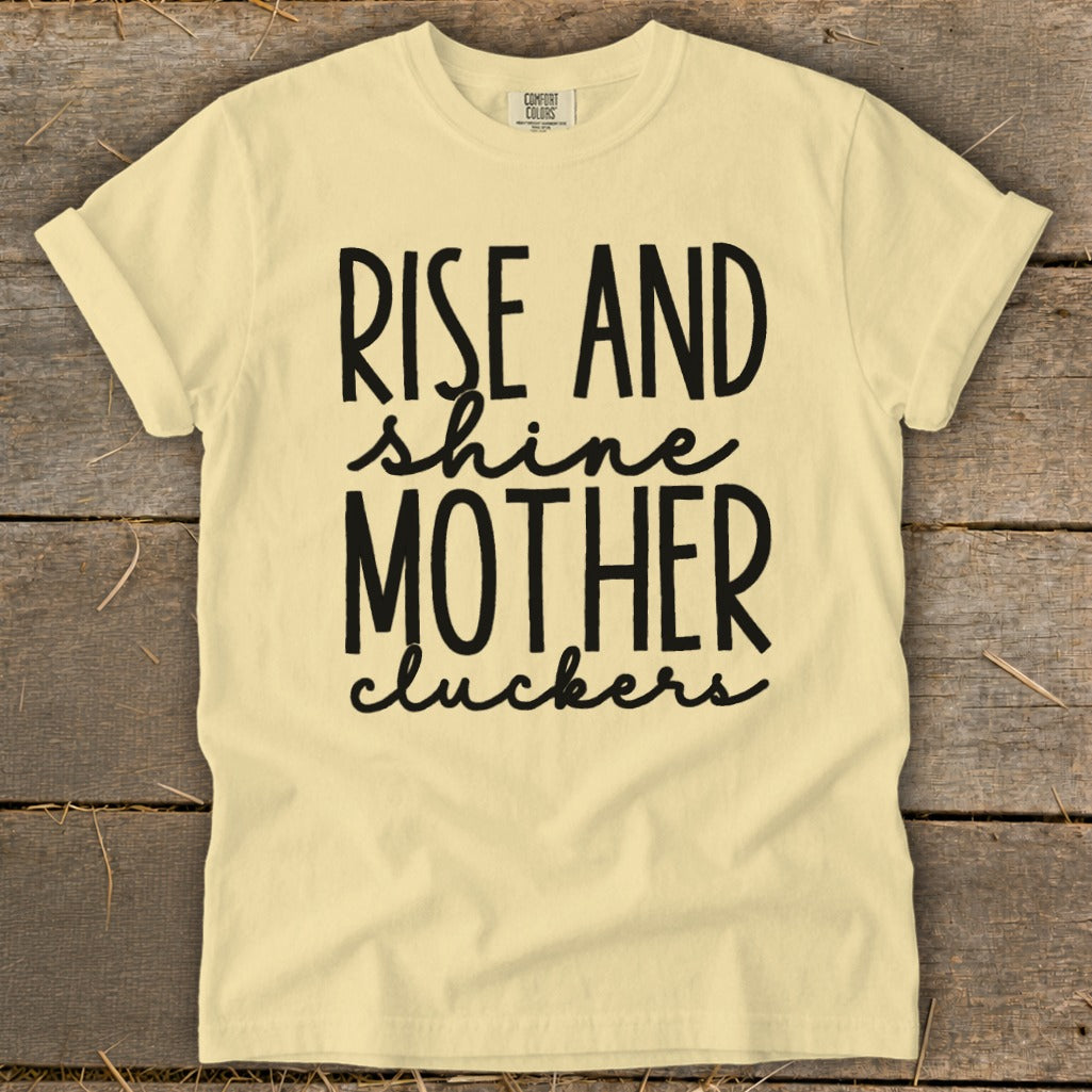 Pale yellow t-shirt with black text: "Rise and shine mother cluckers".