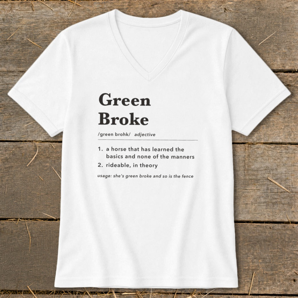 A white V-neck t-shirt with black text defining the term green broke laid flat on a wooden surface.