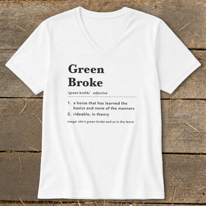 A white V-neck t-shirt with black text defining the term green broke laid flat on a wooden surface.