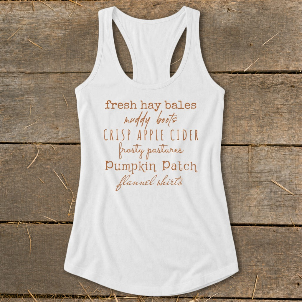White tank top with fall phrases: fresh hay bales, muddy boots, crisp apple cider, frosty pastures, pumpkin patch, flannel shirts.