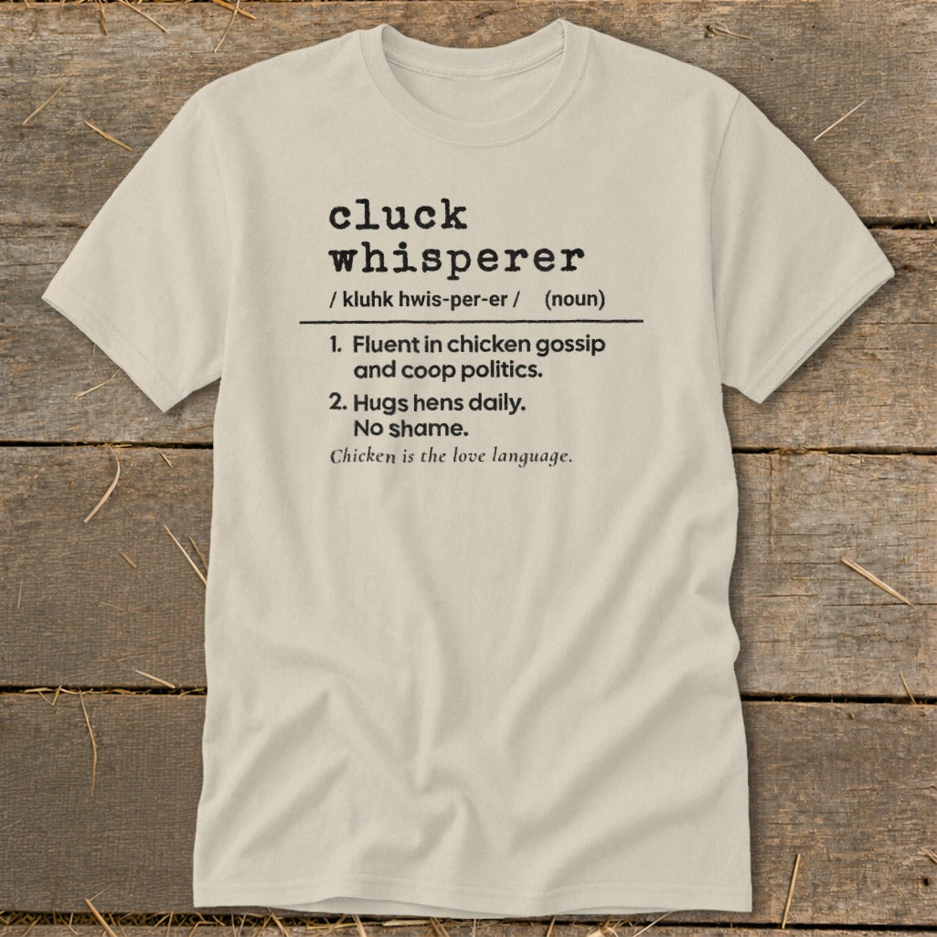 Cream t-shirt with black text defining "cluck whisperer" for chicken lovers.